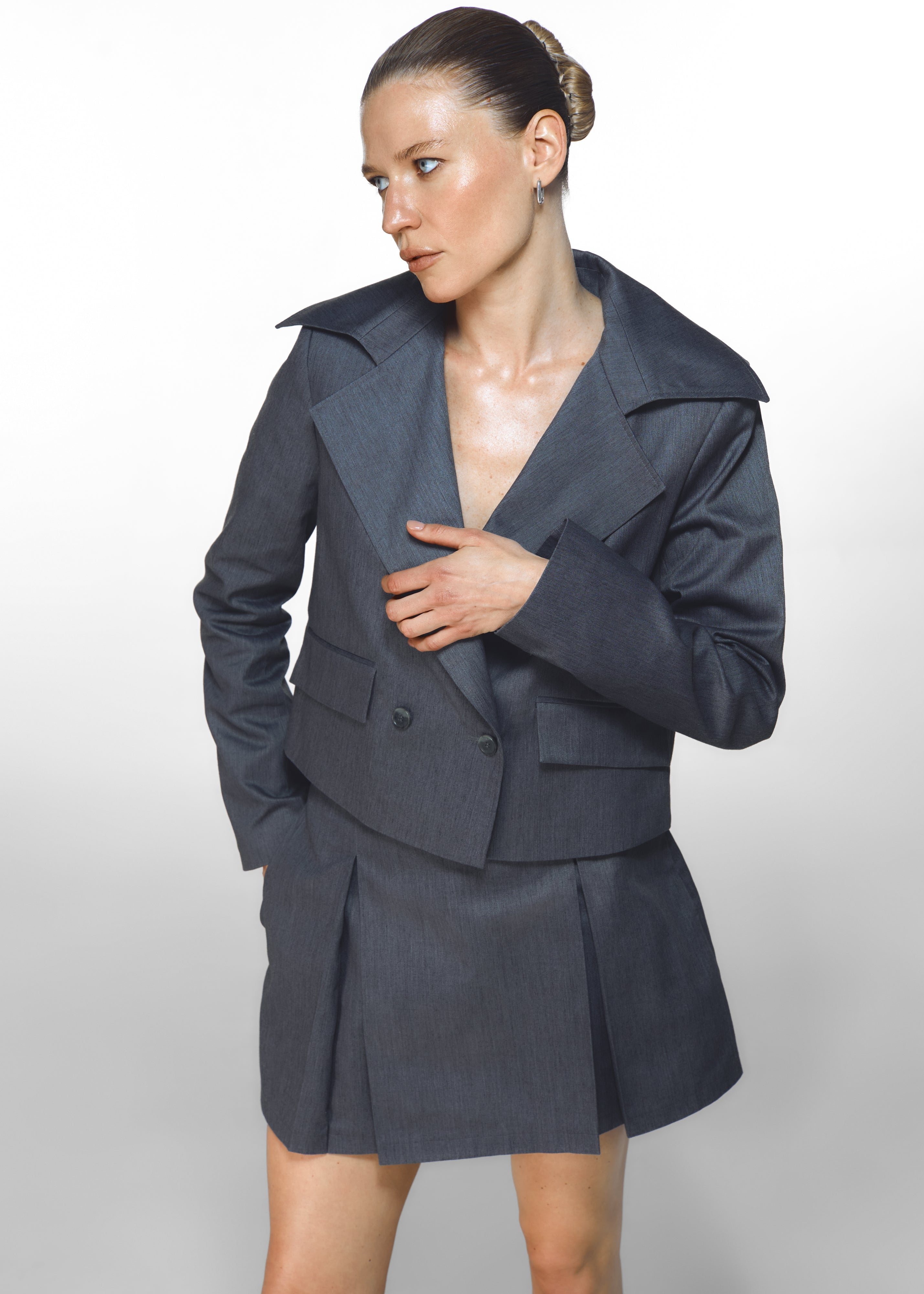 A girl posing in HER CIPHER recycled polyester and organic cotton jacket and skirt in color Graffite