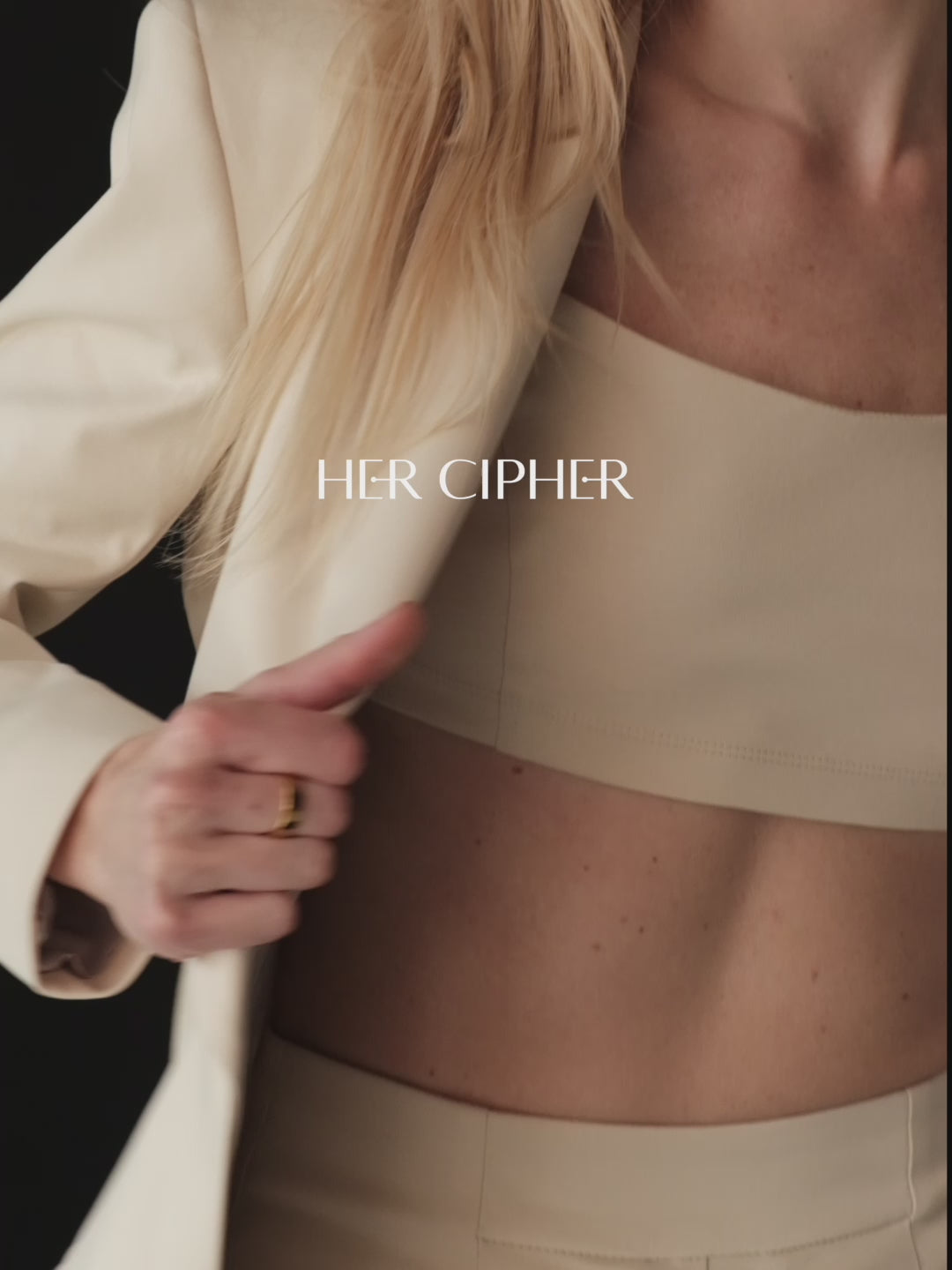 A model posing wearing a set of three organic clothing items:crop top, wide-leg pants and a fitted blazer in light beige color