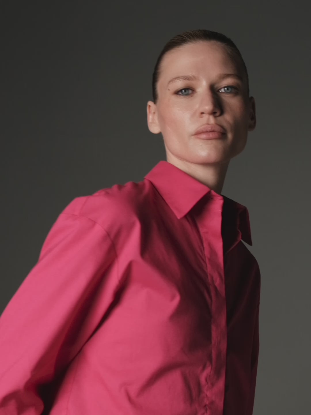 A model slowly posing wearing an organic cotton magenta cropped shirt and a pleated grey mini skirt