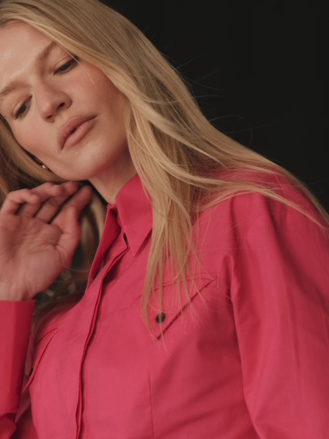 A model posing wearing a bright magenta fitted shirt made of sustainable organic cotton