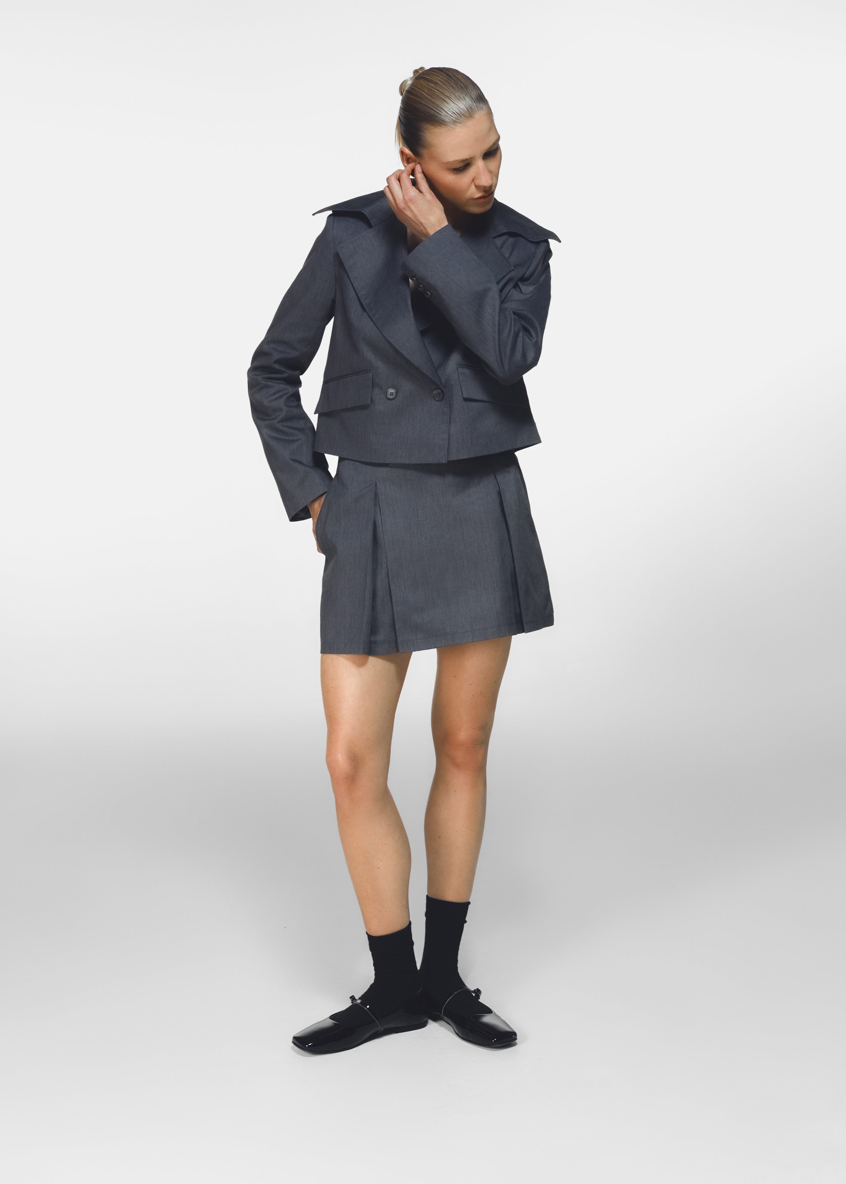A model posing wearing HER CIPHER jacket and mini skirt set created from recycled polyester and organic cotton