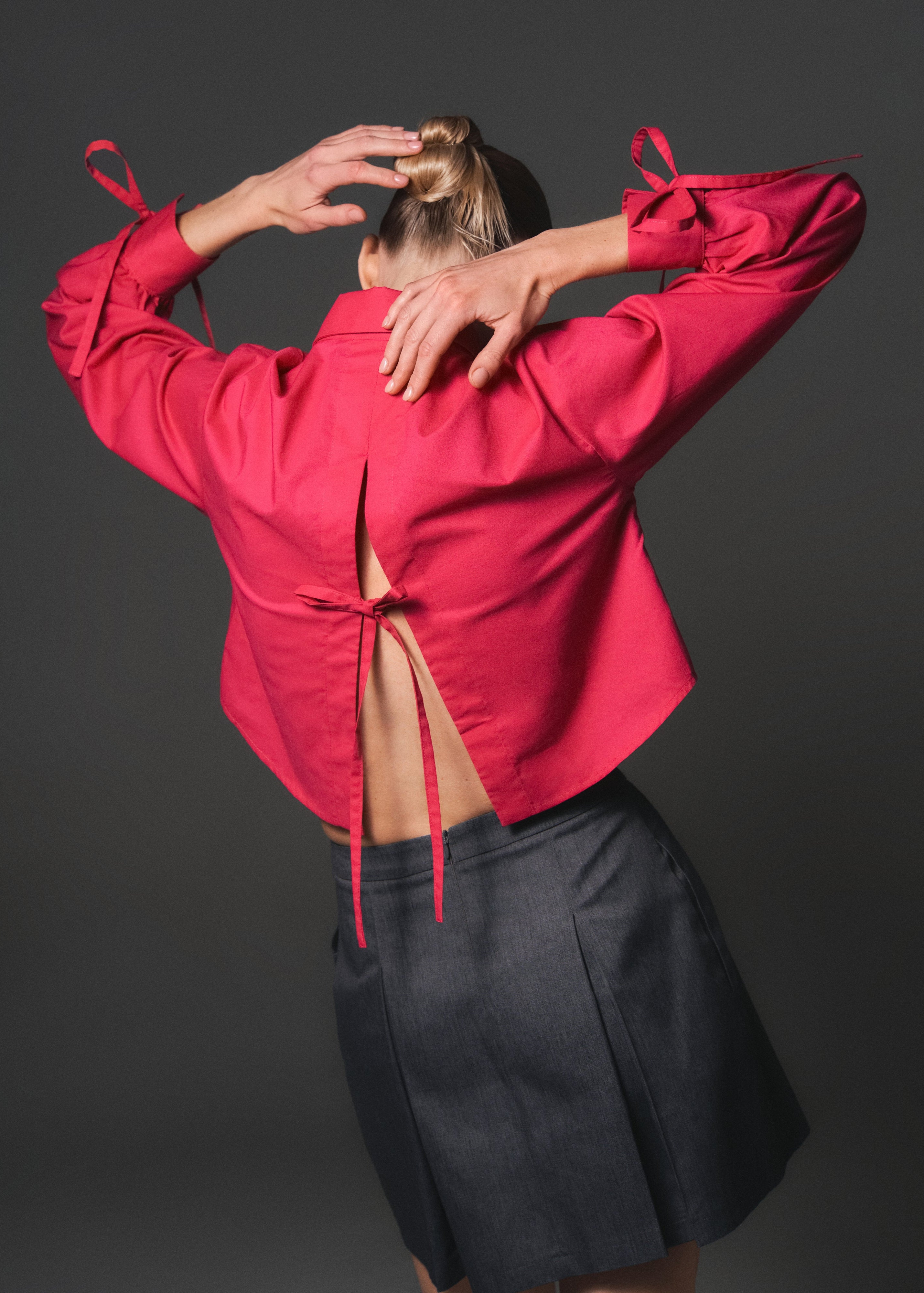 A model posing from the back wearing a magenta color cropped shirt with a slit and three bow-tie details