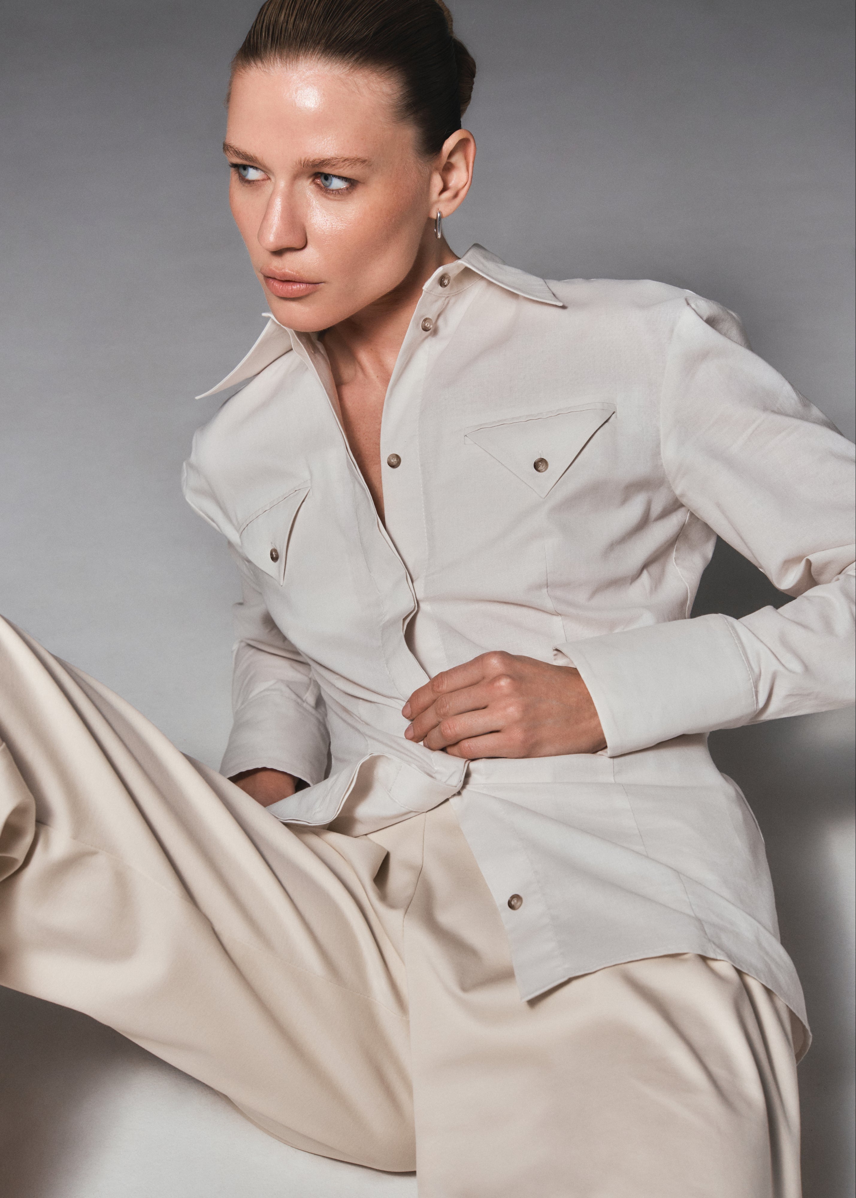 A model sitting and posing wearing a sustainable organic cotton shirt and pants by HER CIPHER, certified with GOTS
