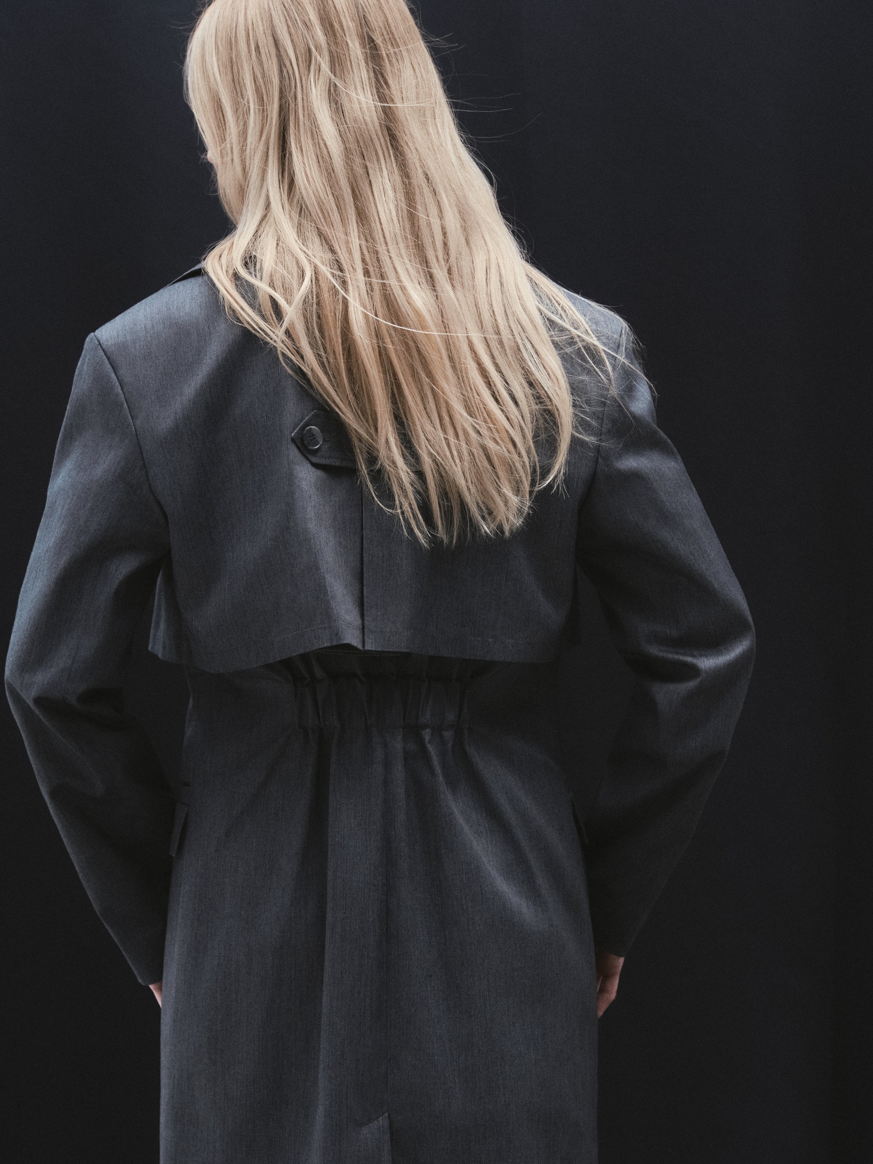A back of a grey trench coat created from recycled polyester with an elastic detail on a waist