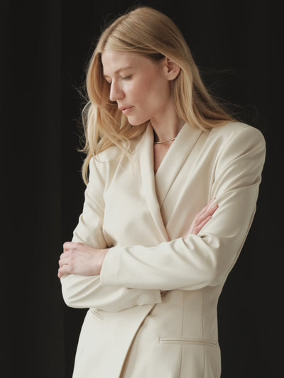 A model posing wearing a light beige organic cotton sustainable blazer and silk maxi skirt