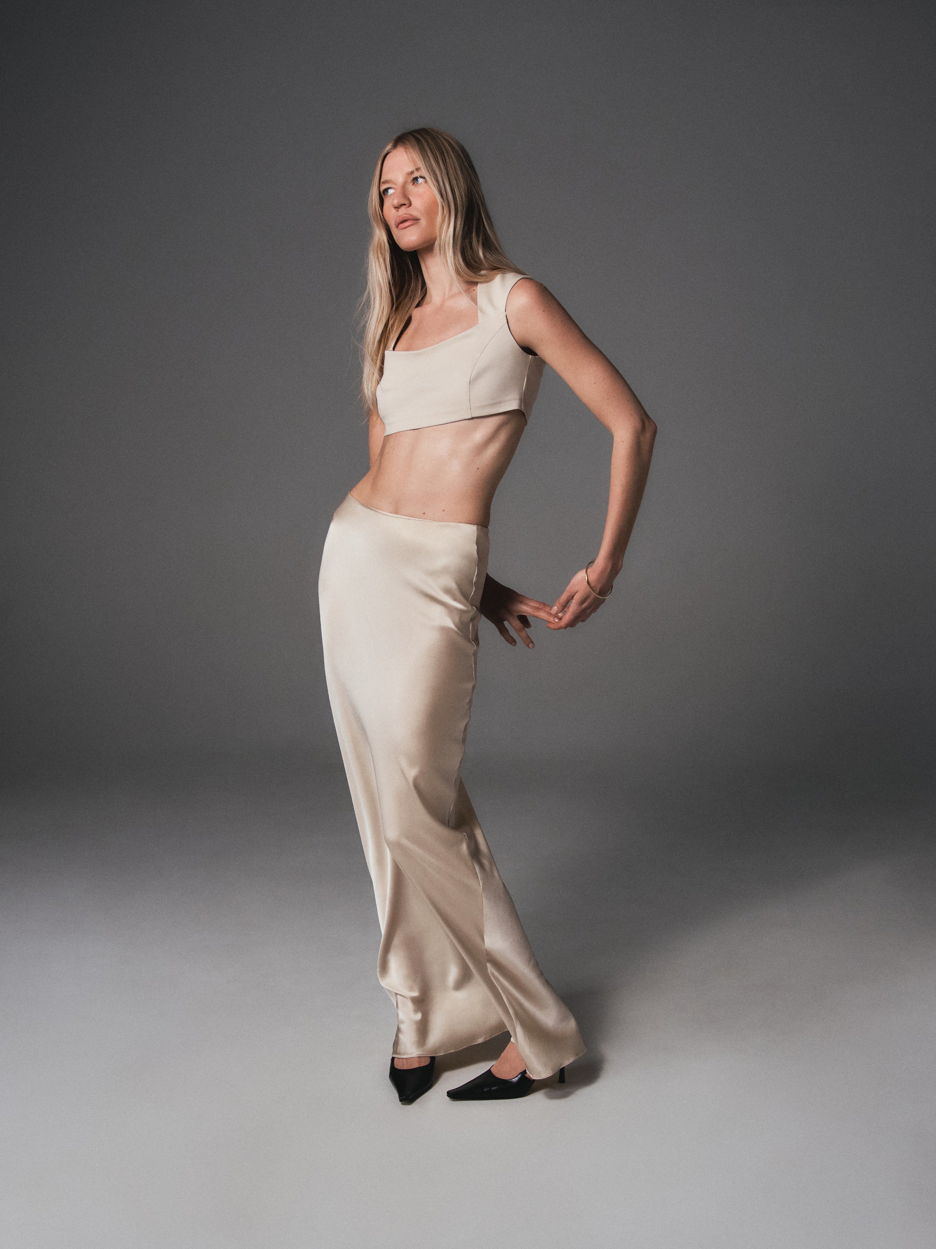 A model posing in a crop top made from organic cotton and a silk maxi skirt in light beige color