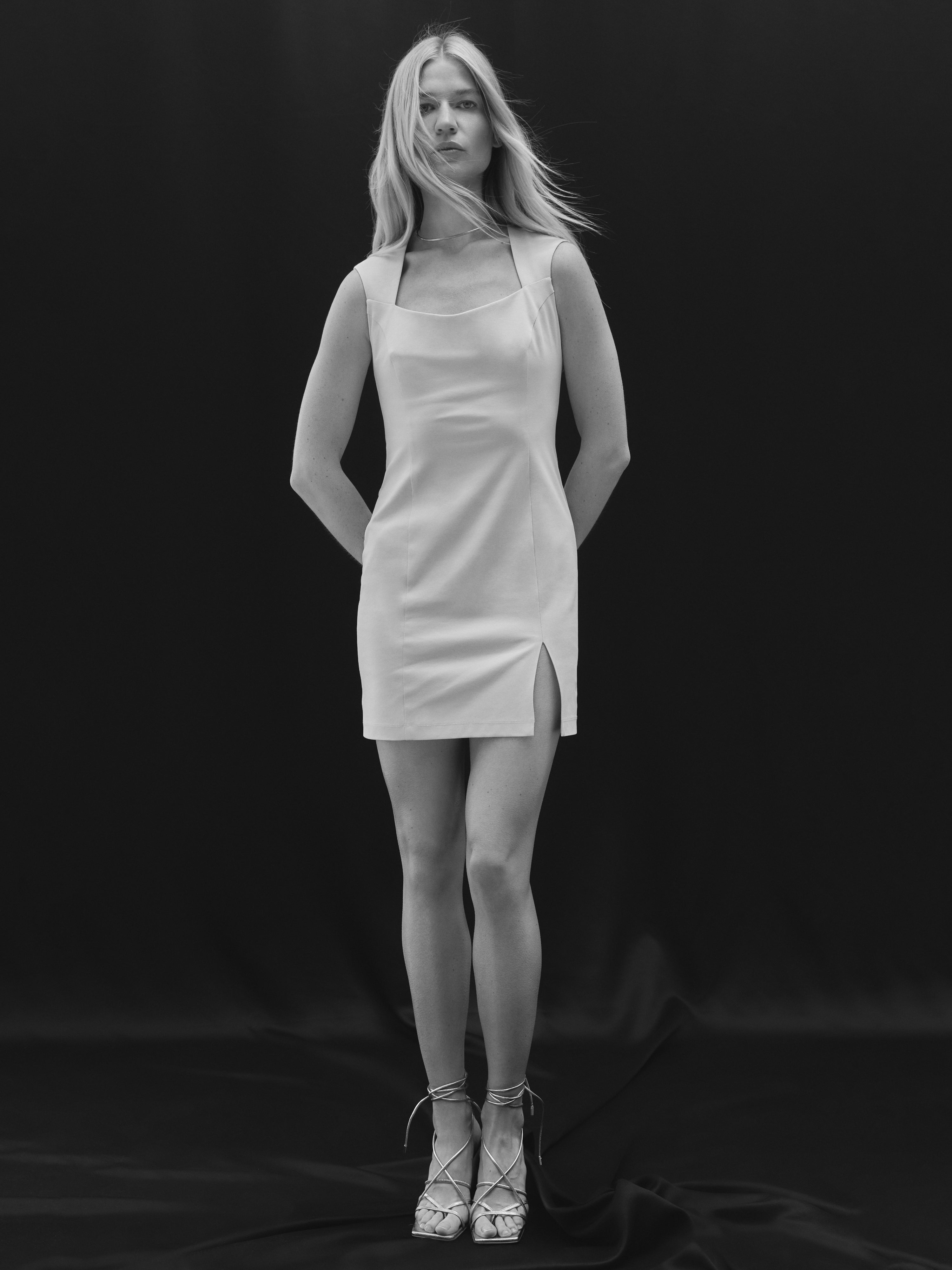 A blond model posing in a light beige mini dress with a front slit by Her Cipher